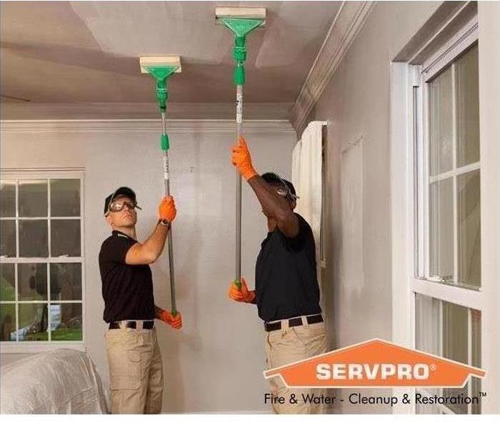 Two SERVPRO technicians cleaning soot off of the ceiling of a room
